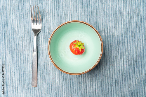 A single strawberry in a bowl as a symbol of a diet