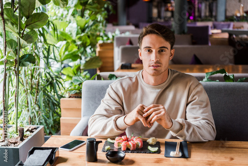 handsome man sitting in sushi bar near tasty meal