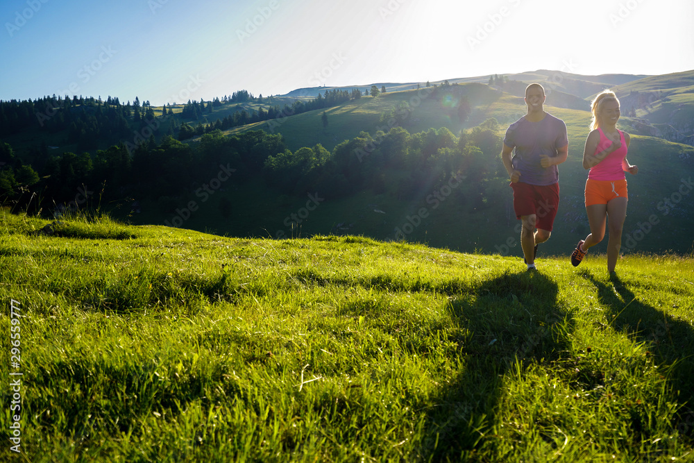 Running fitness couple of runners doing sport on road outdoor. Active living man and woman jogging training cardio in summer outdoors nature.