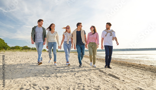 friendship, leisure and people concept - group of happy friends walking along beach in summer