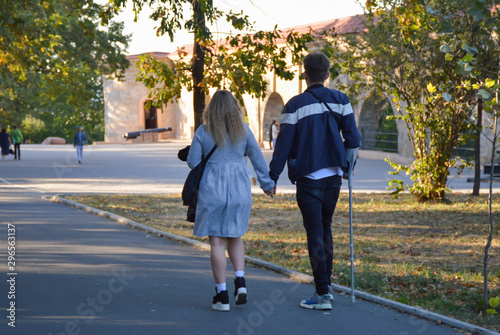 Vászonkép A girl and a guy with a crutch walk in the park