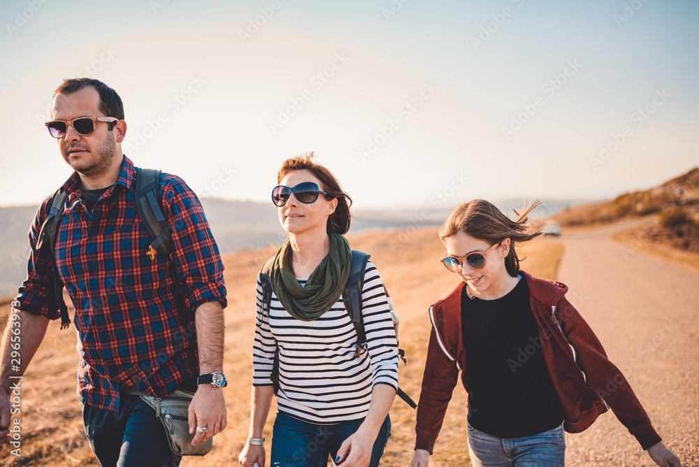 Family hiking together by the asphalt road on a sunny day