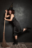 Full length image of witch girl in halloween costume holding broom