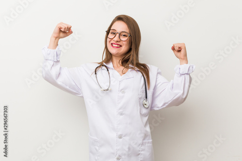 Young doctor woman against a white wall showing strength gesture with arms  symbol of feminine power