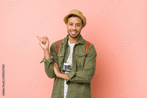 Young filipino traveler man smiling cheerfully pointing with forefinger away.