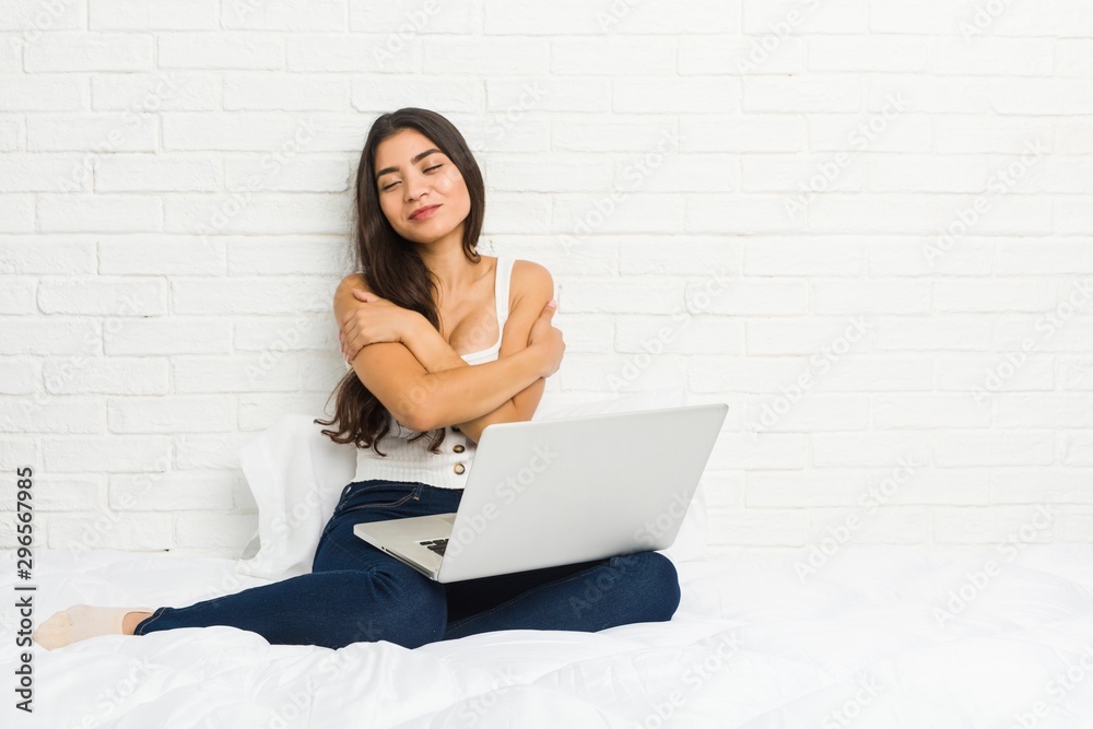 Young arab woman working with her laptop on the bed hugs, smiling carefree and happy. Young arab woman working with her laptop on the bed hugs, smiling carefree and happy.