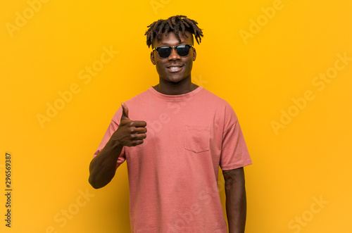 Young casual black man wearing sunglasses smiling and raising thumb up