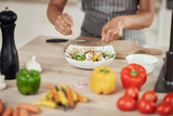 Close up of mixed race woman in apron mixing vegetables in bowl while standing in kitchen at home.