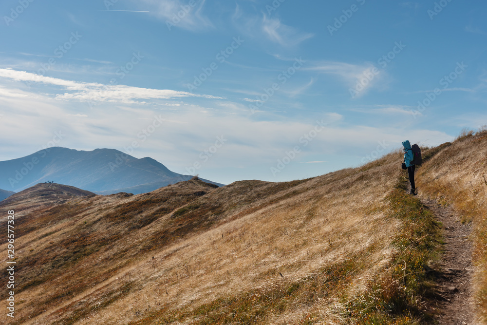 Young girl travels through beautiful mountain ranges with fantastic views of autumn meadows and peaks