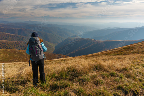 Young girl travels through beautiful mountain ranges with fantastic views of autumn meadows and peaks