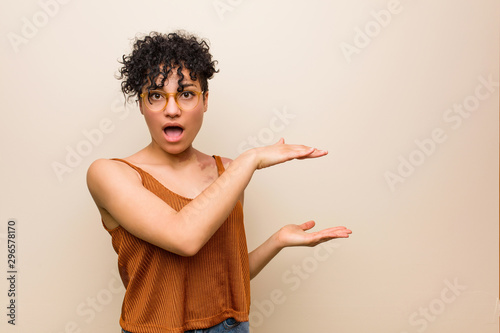Young african american woman with skin birth mark shocked and amazed holding a copy space between hands.