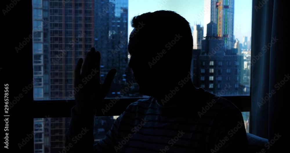 A backlit man gives an anonymous interview in front of a hotel window with the Manhattan skyline in the background.  	