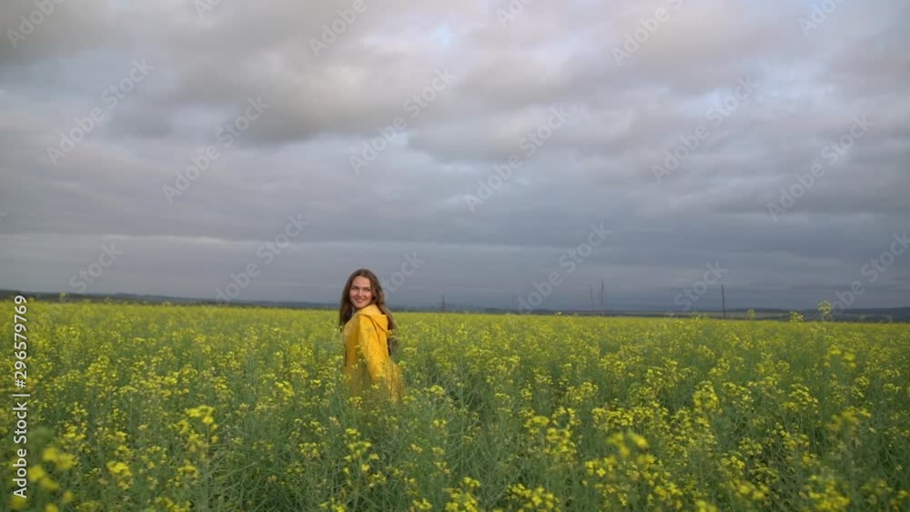 Yellow. A beautiful young girl in a yellow raincoat walks through a field of yellow flowers. Looks at the camera. Summer sunny day. Yellow. A beautiful young girl in a yellow raincoat walks through a field of yellow flowers. Looks at the camera. Summer sunny day.
