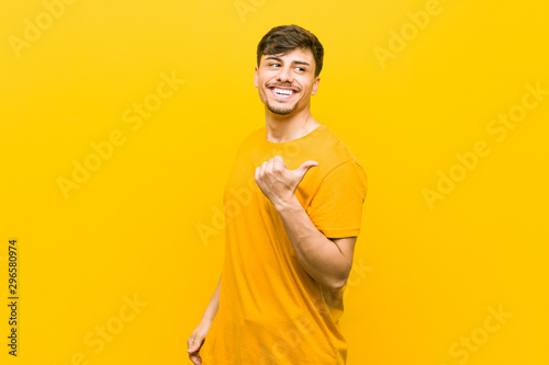 Young hispanic casual man points with thumb finger away, laughing and carefree.