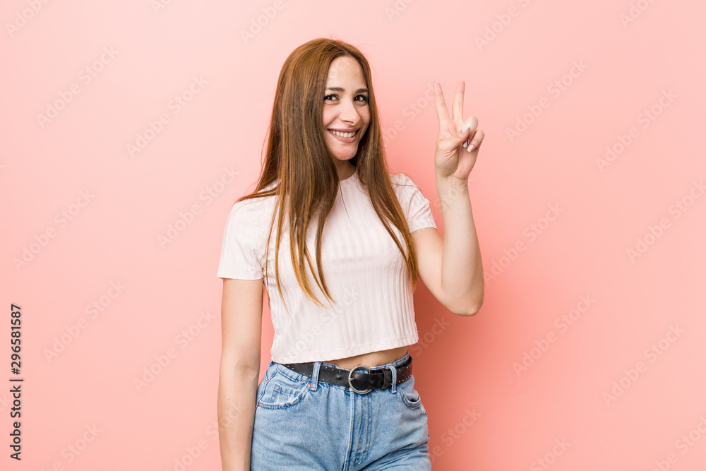 Young redhead ginger woman against a pink wall showing victory sign and smiling broadly. Young redhead ginger woman against a pink wall showing victory sign and smiling broadly.