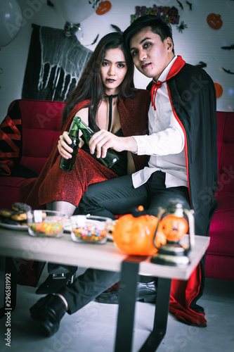 Happy couple of love in Halloween costume and makeup celebrating and drinking beer in Halloween night party