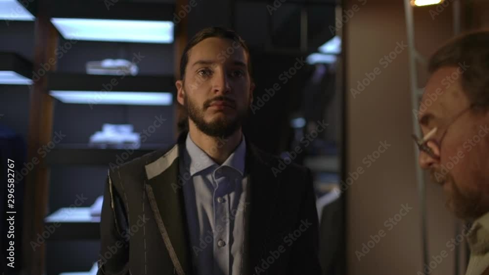 Handsome businessman standing in atelier as old bearded skilful tailor