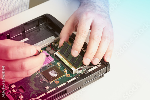 Man repairs computer. A service engineer in shirt repairs laptop, at white Desk against white wall.