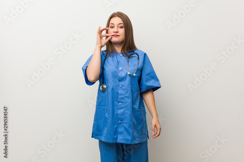 Young nurse woman against a white wall with fingers on lips keeping a secret.