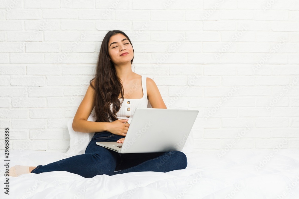 Young arab woman working with her laptop on the bed touches tummy, smiles gently, eating and satisfaction concept. Young arab woman working with her laptop on the bed touches tummy, smiles gently, eating and satisfaction concept.