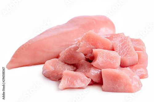 A pile of cut up uncooked boned chicken breast next to whole chicken breast isolated on white.