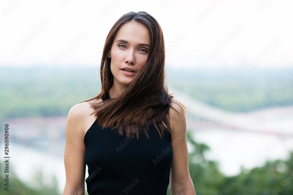 Young pretty likable cheerful woman posing summer city outdoor in Kyiv, Ukraine. Beautiful self-confident girl with long brown hair posing on Dnipro river bank enjoing her life, urban lifestyle