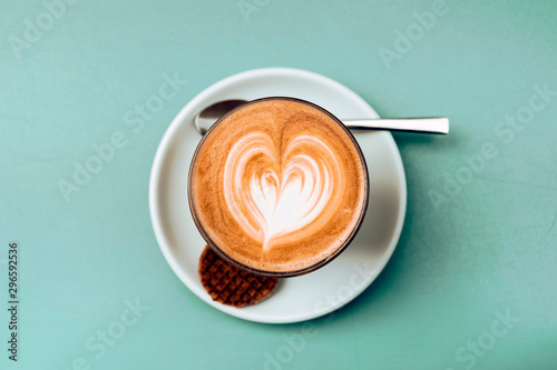 high angle view and close up of a cappuccino cup with teaspoon and cookie against a green background