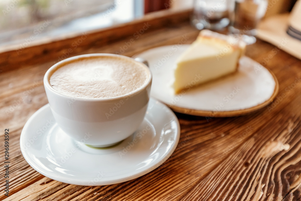 A Cup of cappuccino with foam in the shape of a heart and a piece of cheesecake on a vintage wooden background in a cafe A Cup of cappuccino with foam in the shape of a heart and a piece of cheesecake on a vintage wooden background in a cafe
