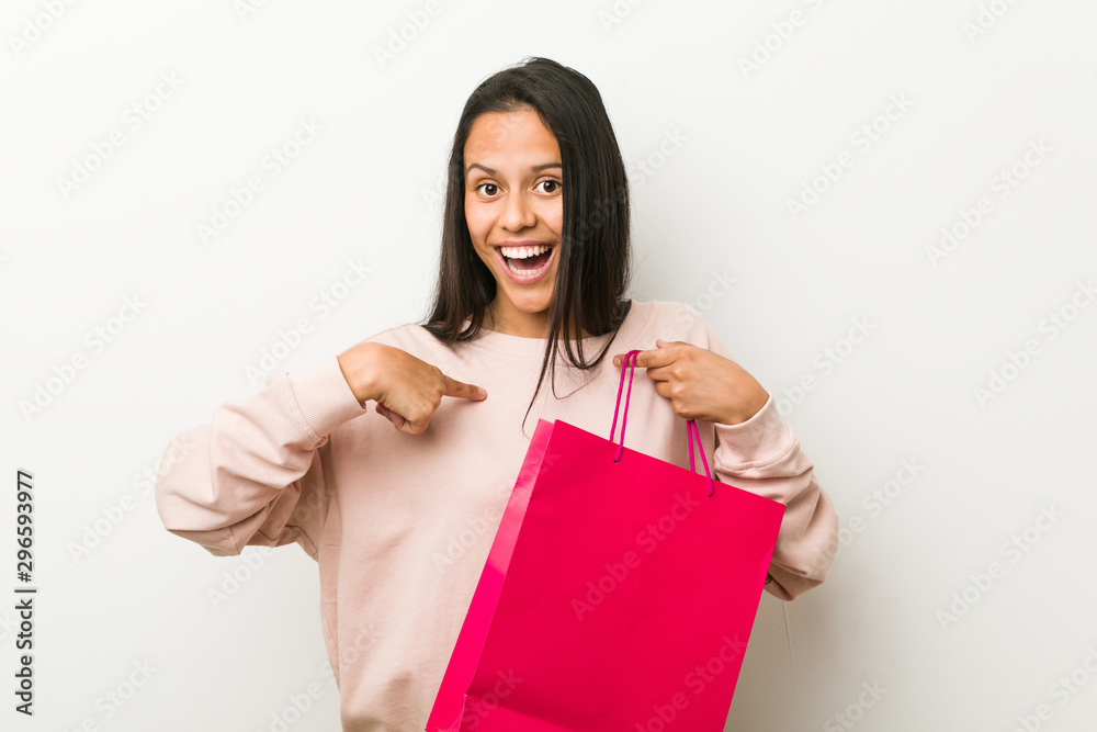 Young hispanic woman holding a shopping bag surprised pointing at himself, smiling broadly. Young hispanic woman holding a shopping bag surprised pointing at himself, smiling broadly.