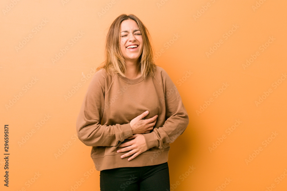 Obraz premium Young authentic charismatic real people woman against a wall laughs happily and has fun keeping hands on stomach.