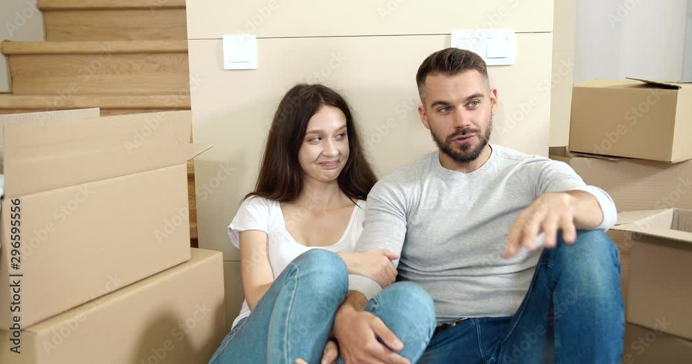 Handsome man and pretty woman sitting on floor in empty apartment and planning future, moving to new home, start of family life
