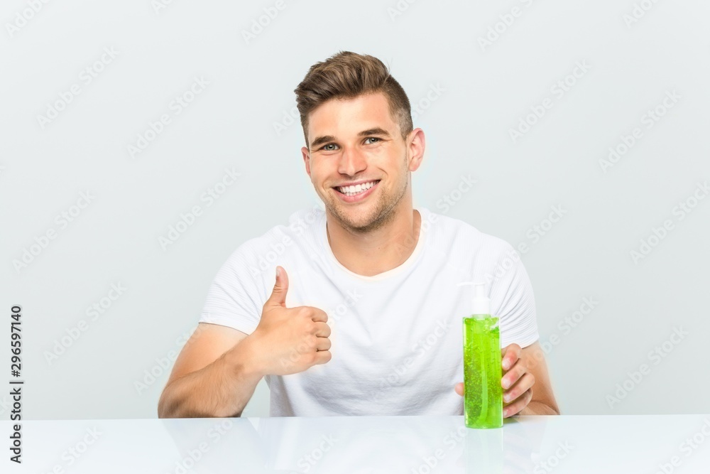 Young handsome man holding a aloe vera bottle smiling and raising thumb up Young handsome man holding a aloe vera bottle smiling and raising thumb up