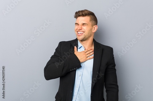 Young handsome caucasian man laughs out loudly keeping hand on chest.