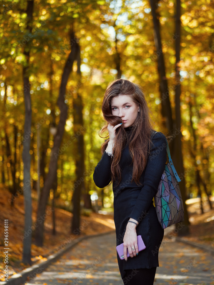 Natural lifestyle outdoors portrait of young adorable redhead woman in black dress with trendy shopper bag emotionally posing in autumn city park with gorgeous golden fall leaves background Natural lifestyle outdoors portrait of young adorable redhead woman in black dress with trendy shopper bag emotionally posing in autumn city park with gorgeous golden fall leaves background