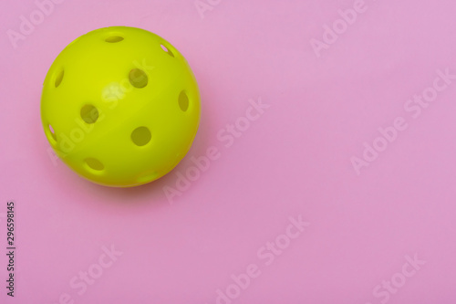 Bright yellow pickleball or whiffle ball on a solid bright pink flat lay background symbolizing sports and activity with copy space.