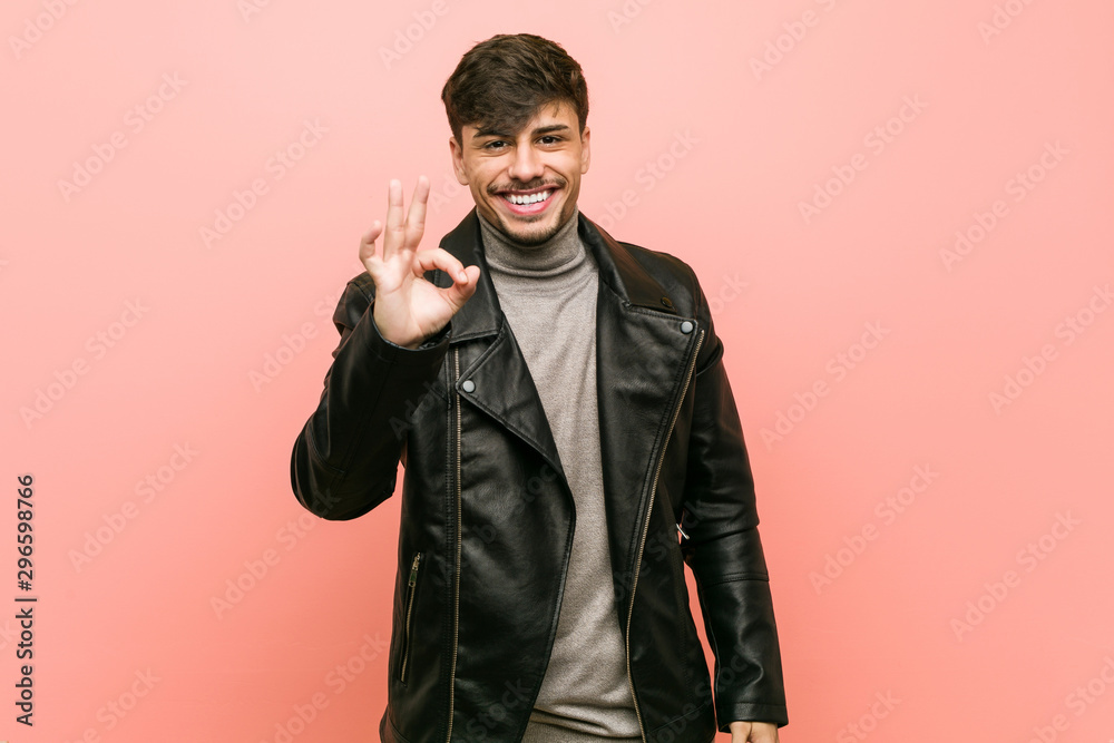 Young hispanic man wearing a leather jacket cheerful and confident showing ok gesture.