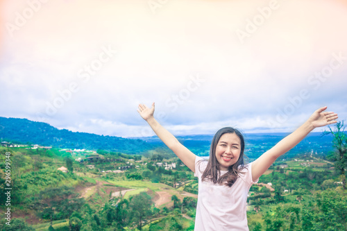 Happy Asian woman stands her arms on a beautiful view of the mountains and the sky