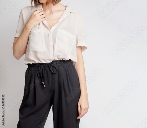 Young woman wearing simple stylish outfit with a neutral shirt and black trousers isolated on light grey background. Copy space