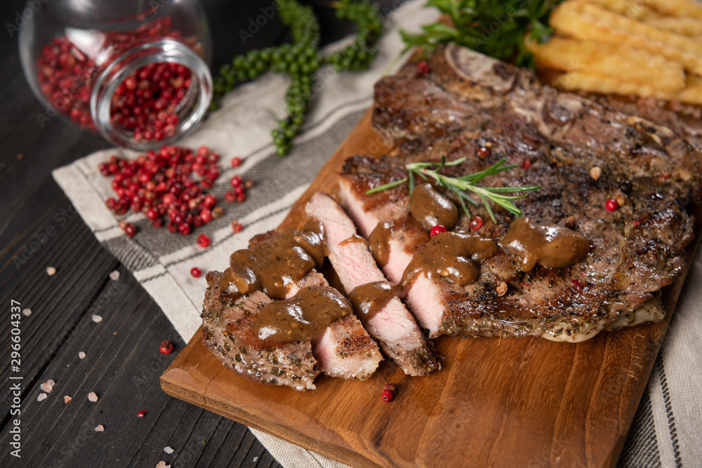Cut of beef steak grilled with dipping sauce served with french frie on chop real wood, no dish and decorate with herb as pepper, pink salt and rosemary. All on the grey dish towel and wood background