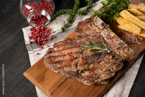 The steak of beef grilled served with french frie placed on chop real wood, no dish and decorate with many herb as pepper, pink salt and rosemary. All placed on the grey dish towel and wood background