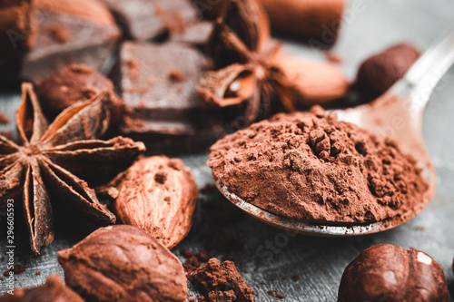 Brown cocoa powder in the spoon, chocolates, star anise and nuts, close-up view, selective focus