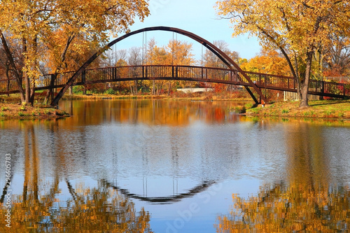 Beautiful fall landscape with stylish bridge in the city park. Scenic view with colored trees and bridge in sunlight reflected in the lake Mendota bay water. Tenney Park, Madison, Wisconsin, USA.