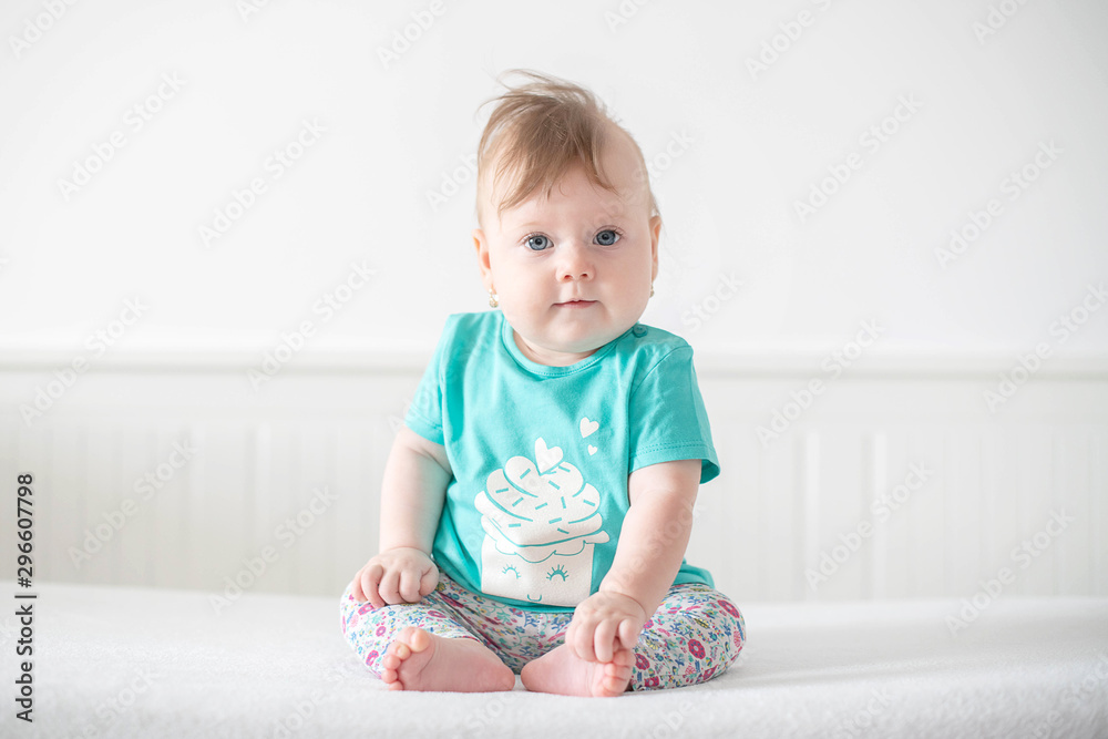 Portrait of adorable Caucasian baby girl with blue eyes, looking at the camera calmly, with curiosity, interactivity or inquisitiveness and sitting in a pristine white baby cot while holding her toes Portrait of adorable Caucasian baby girl with blue eyes, looking at the camera calmly, with curiosity, interactivity or inquisitiveness and sitting in a pristine white baby cot while holding her toes