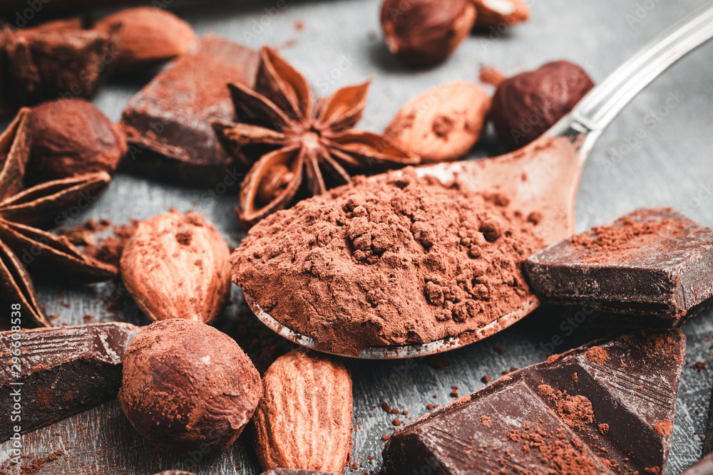 Brown cocoa powder in the spoon, chocolate cubes, star anise and nuts, close-up view, selective focus Brown cocoa powder in the spoon, chocolate cubes, star anise and nuts, close-up view, selective focus