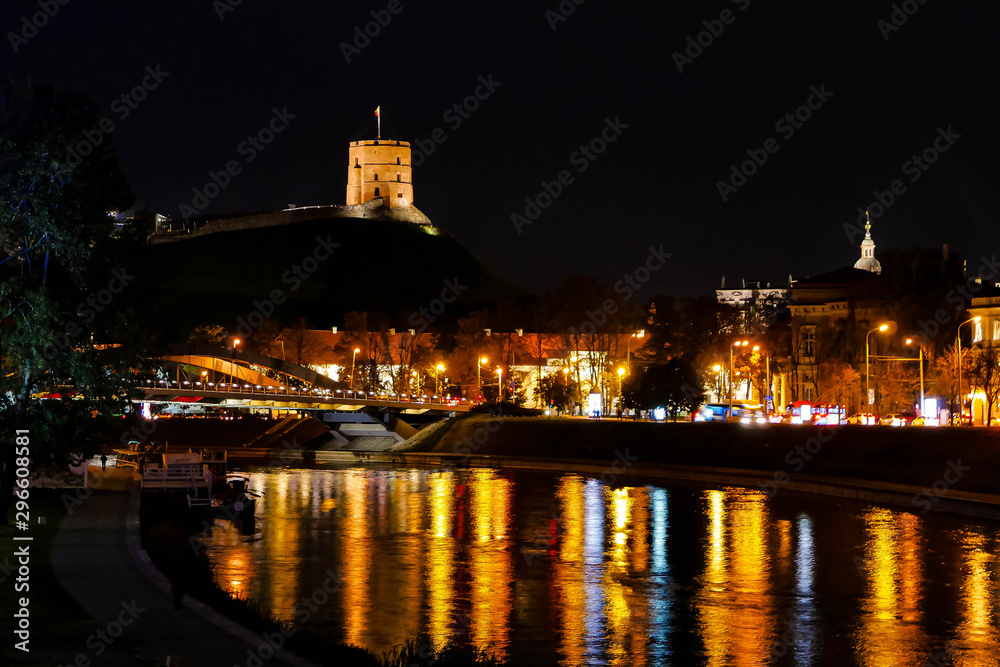 Reflections on Neris river with Gediminas Tower in Vilnius Lithuania and Mindaugas Bridge at night in the foreground