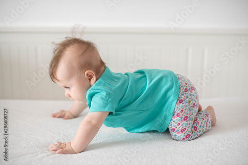 Adorable Caucasian baby girl with blue eyes trying to stand up and walk, focused on the effort and progress; cute baby facial expressions and learning steps or motherhood and family concepts