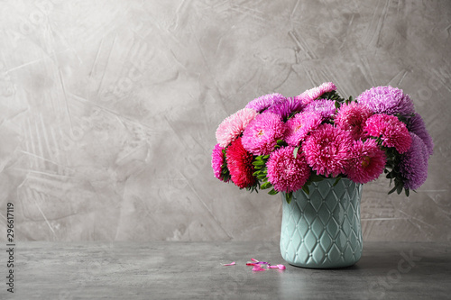 Vase with beautiful aster flowers on grey table against beige background. Space for text photo