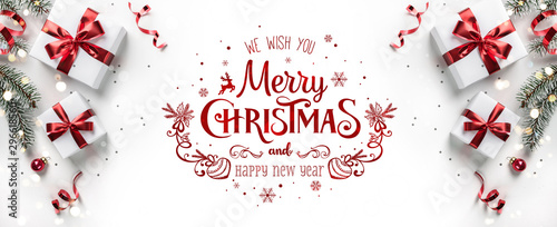 Merry Christmas text on white background with gift boxes, ribbons, red decoration, fir branches, bokeh, sparkles and confetti. Xmas and New Year greeting card, bokeh, light. Flat lay, top view