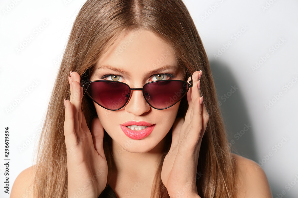 Young woman wearing stylish sunglasses on light background Young woman wearing stylish sunglasses on light background