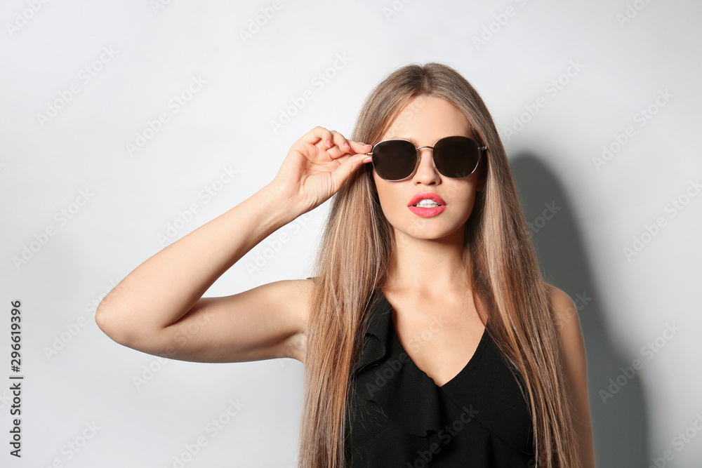 Young woman wearing stylish sunglasses on light background